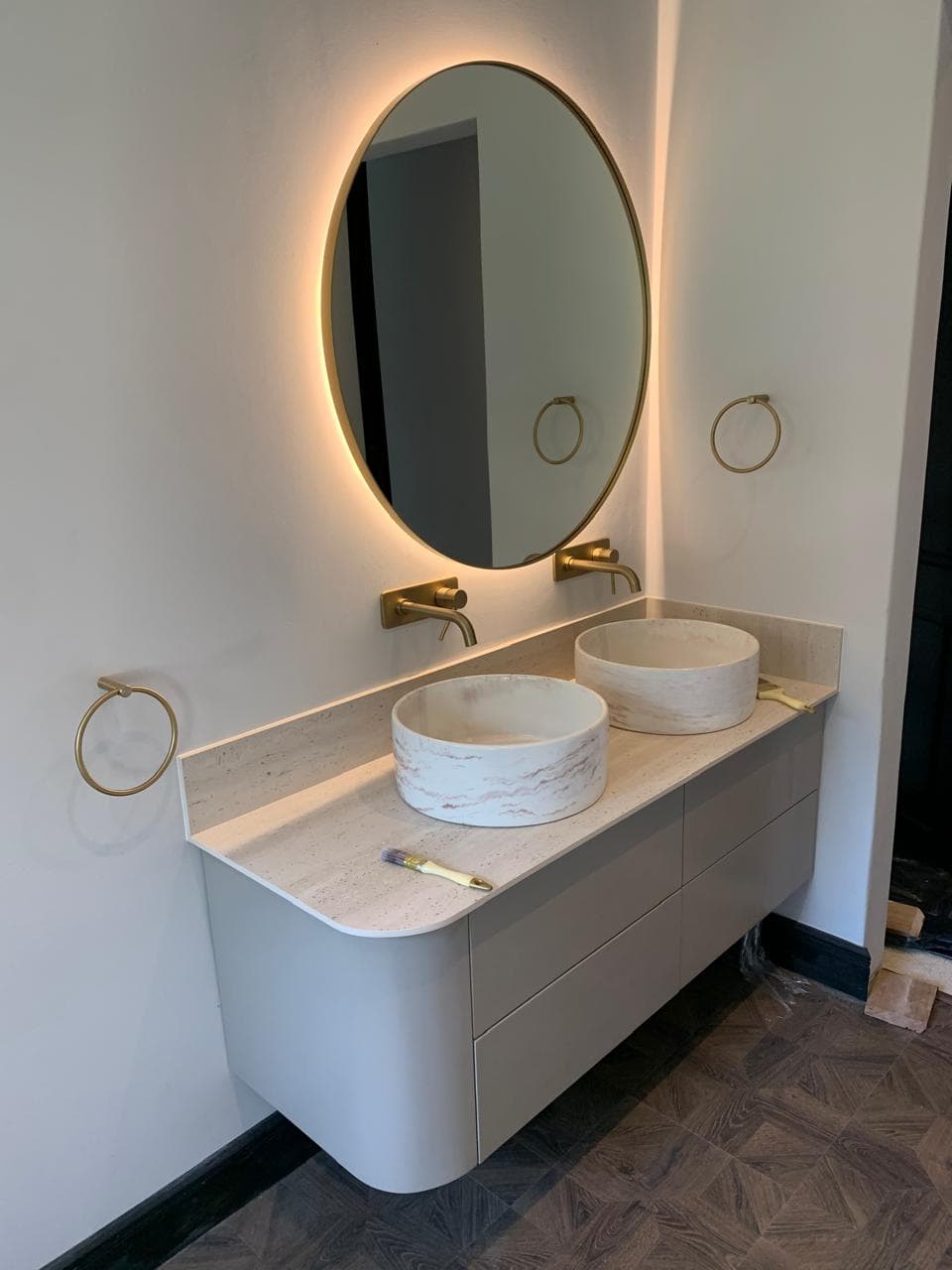 Curved floating vanity with two round basins under a back-lit brass mirror